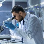 férfi mikroszkóppal vizsgál valamit egy laborban